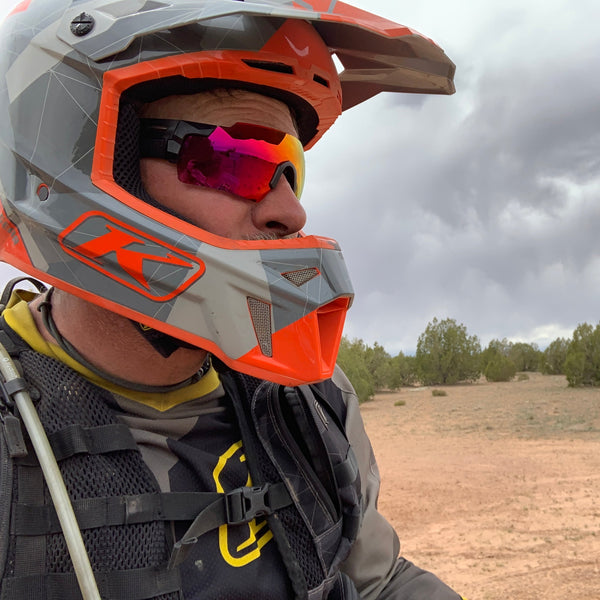 Close-up of a person wearing a helmet with a reflective surface showing clouds and trees.